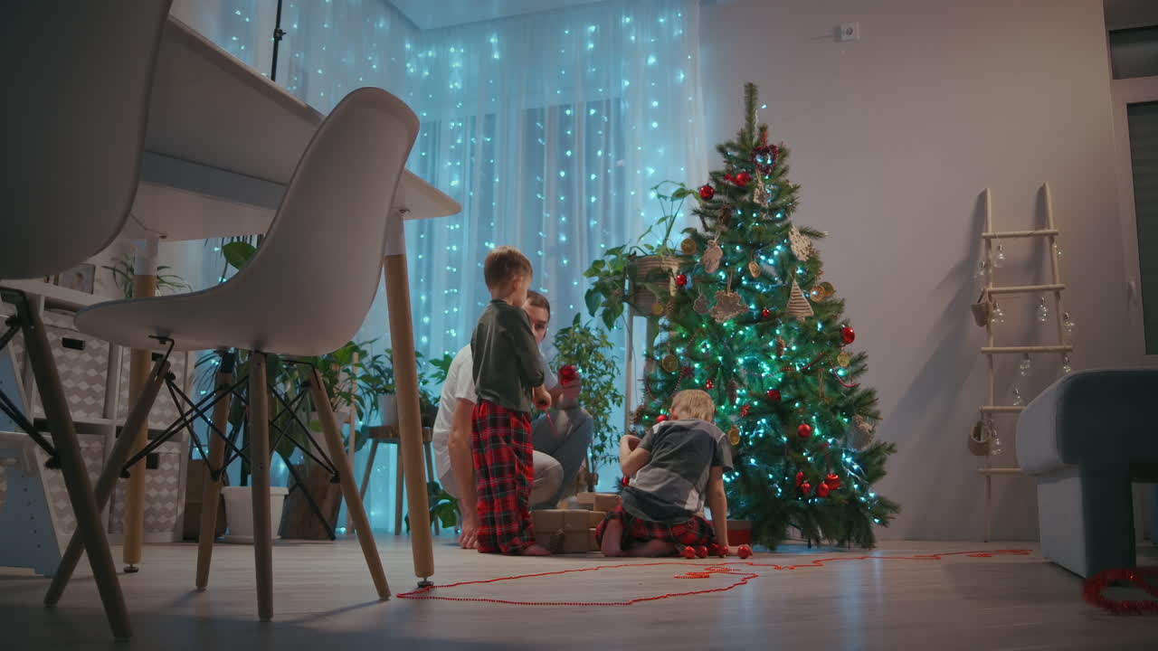 padre y dos niños decoran el árbol de navidad en la víspera de año nuevo y navidad. imágenes de alta calidad 4k