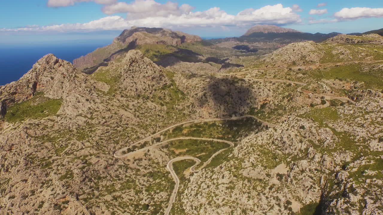 Vista aerea dall'alto di una strada di montagna tortuosa, ombre delle nuvole e il mare in lontananza a Maiorca