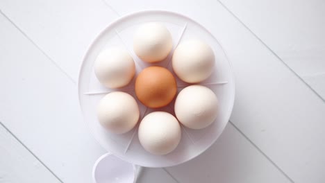 Chicken-eggs-in-a-egg-electric-cooker-on-a-white-wooden-table