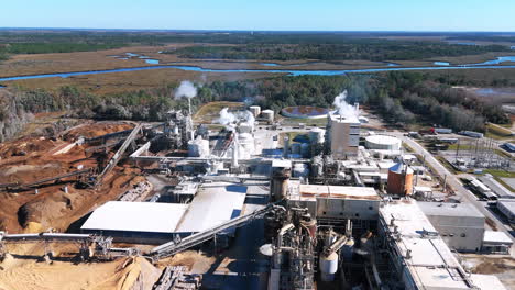 aerial footage during the day rotating around an industrial paper plant that has smoke stacks and is in operation