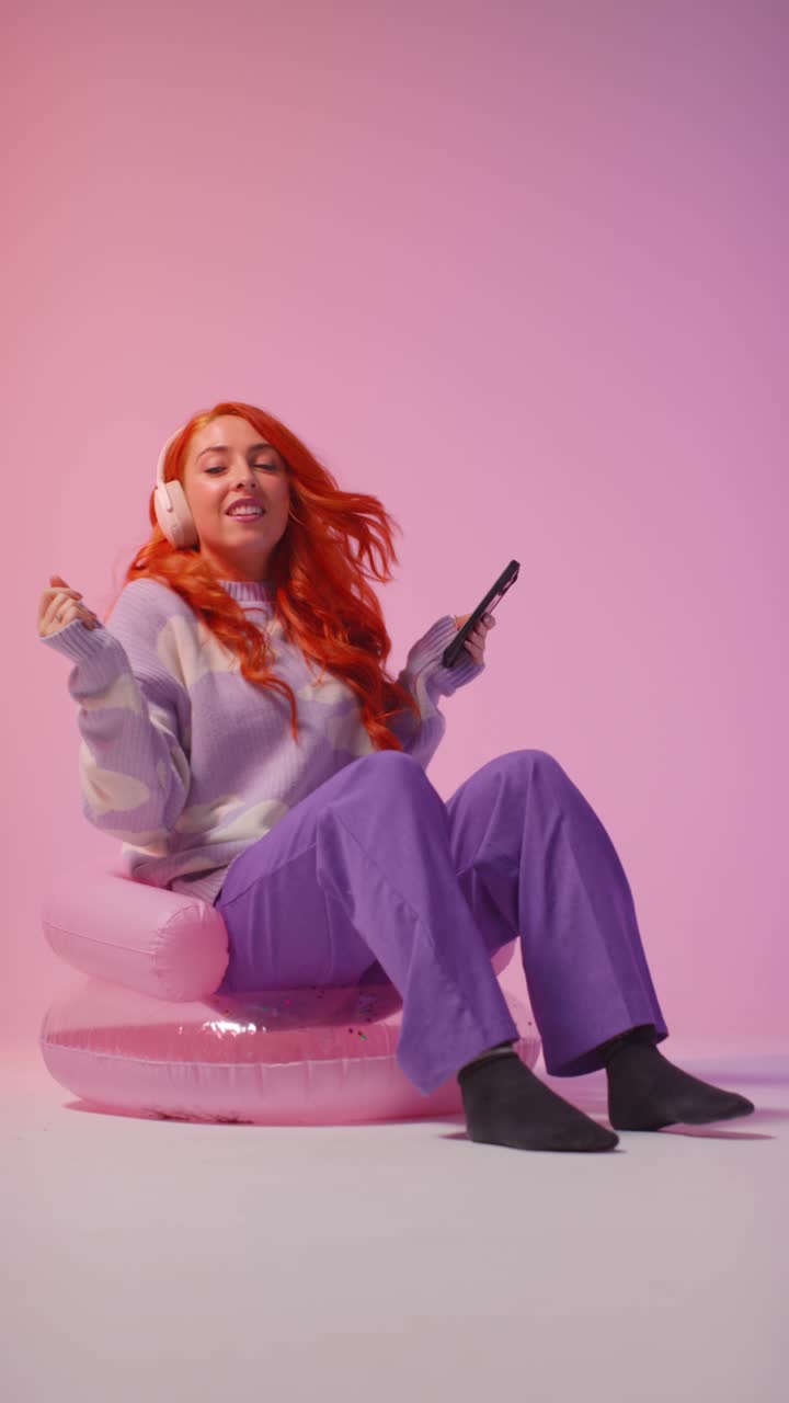 video in studio verticale di una giovane donna della generazione z che indossa le cuffie che trasmette musica al cellulare 2