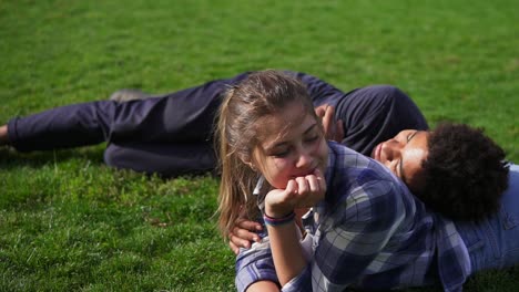 Handsome-african-guy-lying-on-the-back-of-his-caucasian-girlfriend-on-the-green-field-and-talking.-multi-ethnic-couple-enjoying