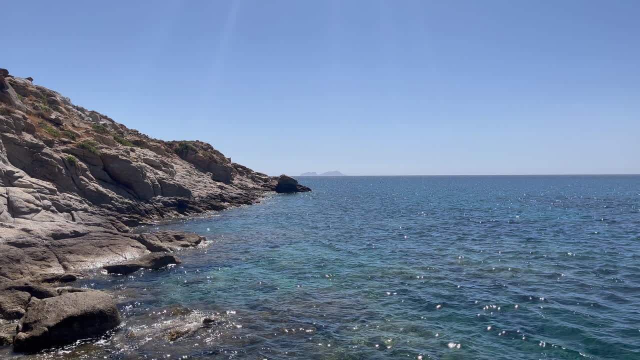 Scenic footage of waves hitting rocky shoreline at Kalafati Beach, Mykonos. Clear blue Aegean Sea, natural coastal beauty, and a serene Mediterranean setting