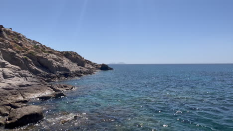 scenic footage of waves hitting rocky shoreline at kalafati beach, mykonos. clear blue aegean sea, natural coastal beauty, and a serene mediterranean setting