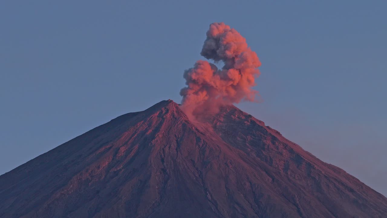 Vulcano Semeru in eruzione con una nuvola di cenere rossa al tramonto.