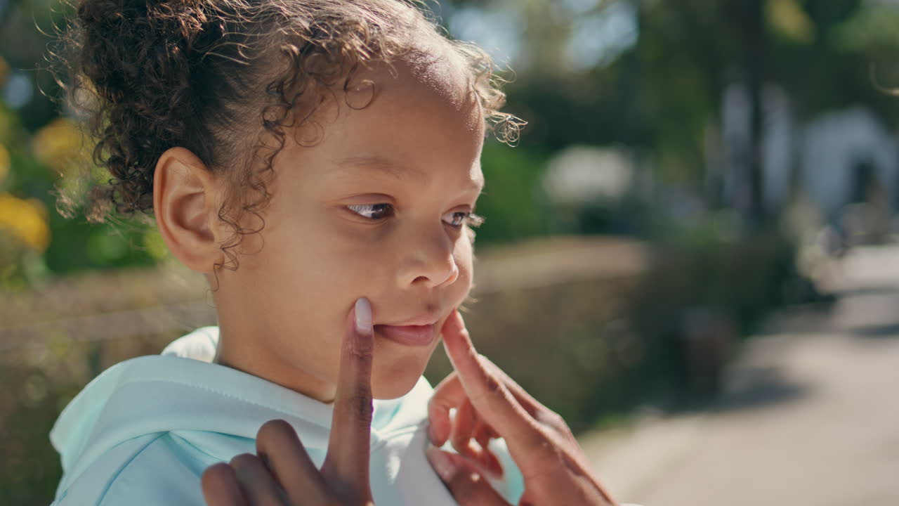 las manos de la madre tocando la cara de la hija haciendo una sonrisa de cerca. niña de pie en el parque