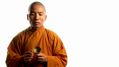 a buddhist monk wearing an orange robe taps a bell with a small stick