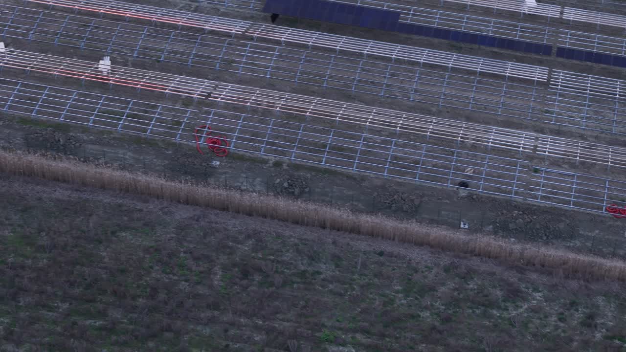 Photovoltaic farm construction progressing in agricultural field, installing rows of solar panels