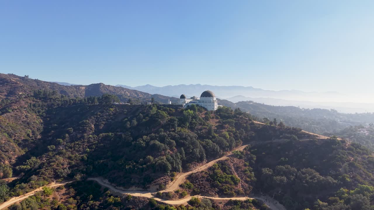 Aerial view of the Griffith Observatory perched above Los Angeles, with trails winding through the Hollywood Hills under a clear morning sky