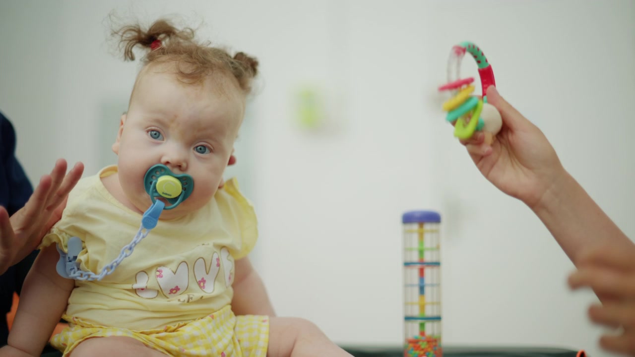 Baby with pacifier engaging in a physical therapy session for developmental assessment, supported by a blurred professional