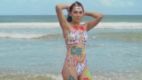 In-the-Caribbean,-a-girl-in-body-paint-and-a-bikini-enjoys-the-sunshine-on-a-white-sand-beach-with-ocean-waves-in-the-background