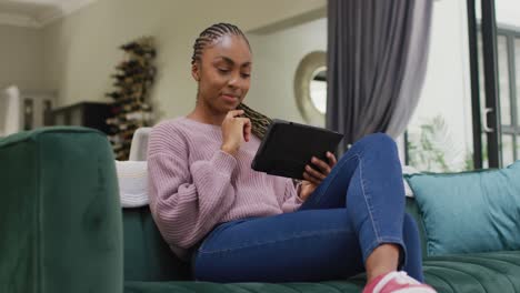 Happy-african-american-woman-using-tablet-and-sitting-on-sofa