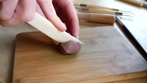un artista cortando y esculpiendo arcilla de modelado marrón suave con una herramienta manual de madera mientras crea un proyecto en su estudio de arte