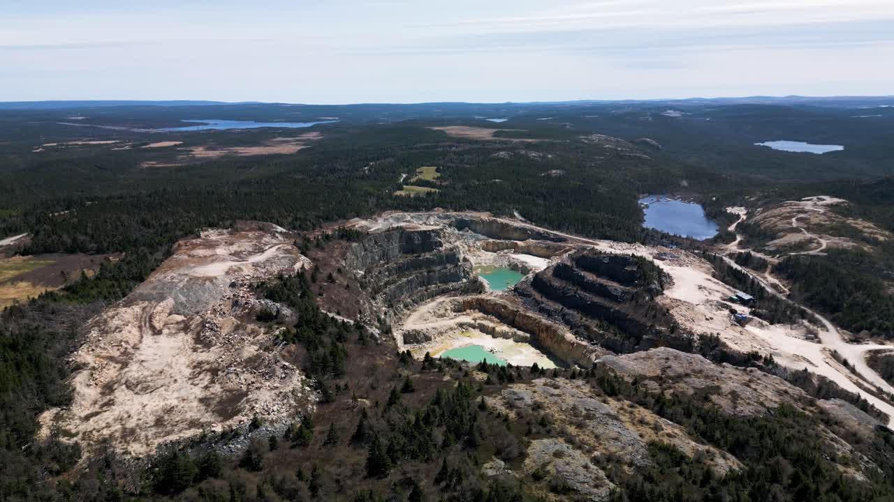 Drone shot of an open talc mine quarry in Manuels, Newfoundland Canada revealing the toxic aquamarine blue water within and the vast wilderness behind
