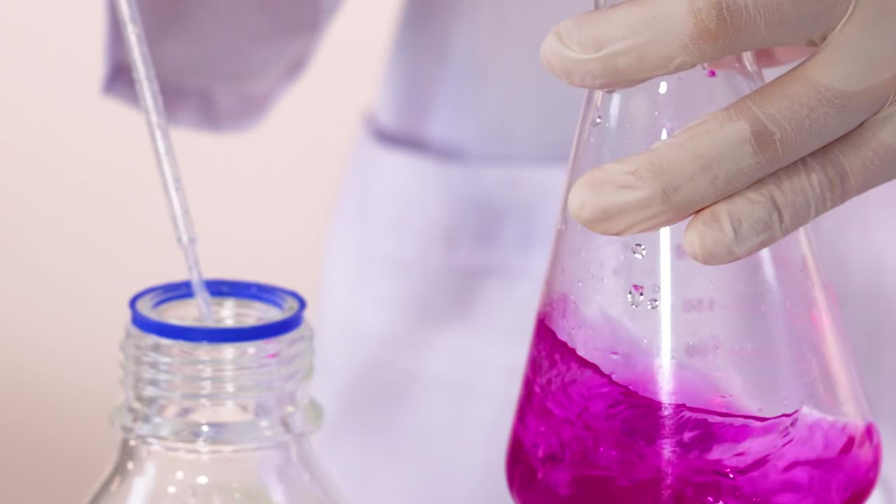 A gloved hand mixes a vibrant pink solution in a laboratory flask using a pipette.