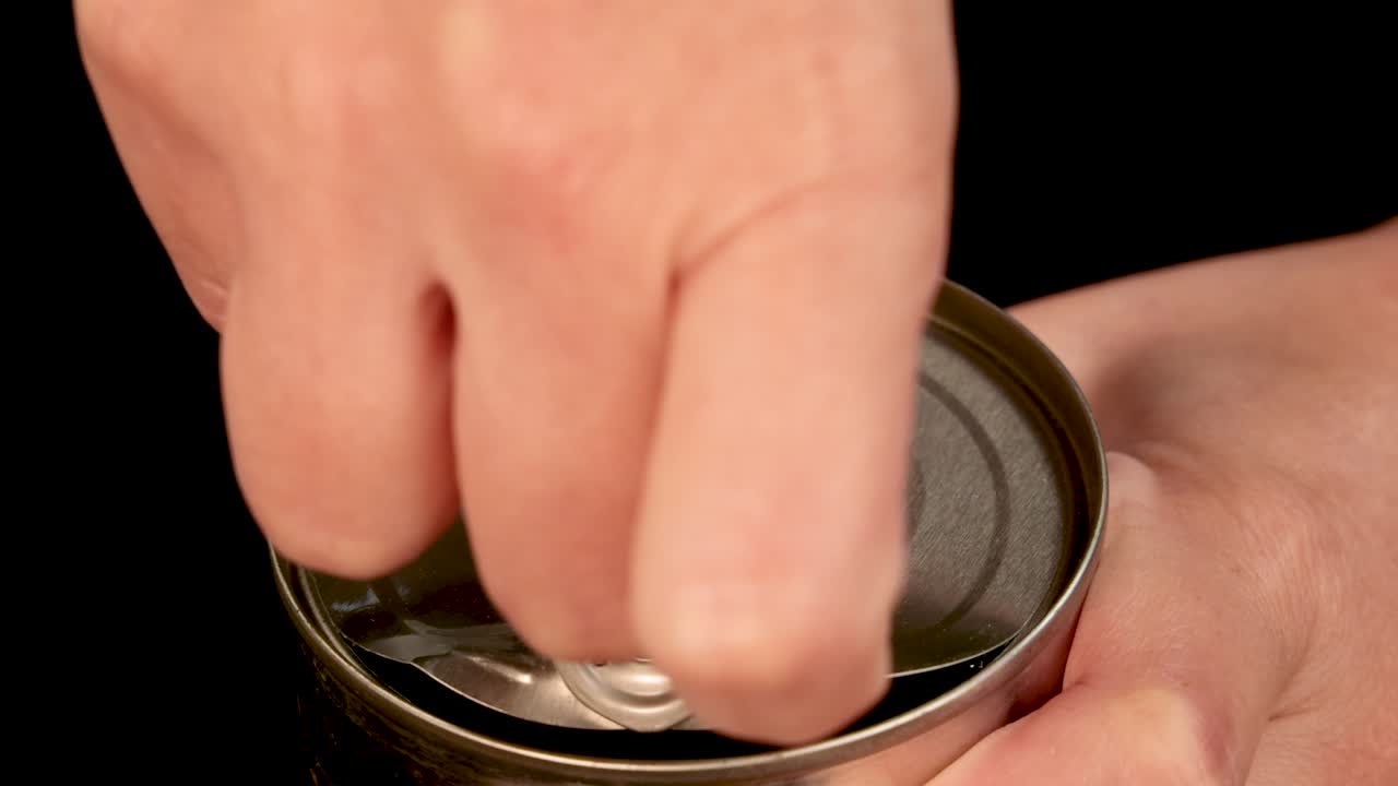 A hand opens a pull-tab can of baked beans in tomato sauce, shot in close-up with even lighting and a black background for clarity