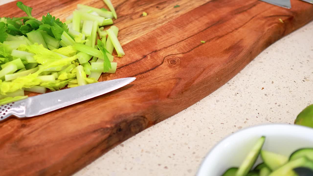 A sequence of fresh vegetables being prepared on a wooden cutting board in a well-lit kitchen setting