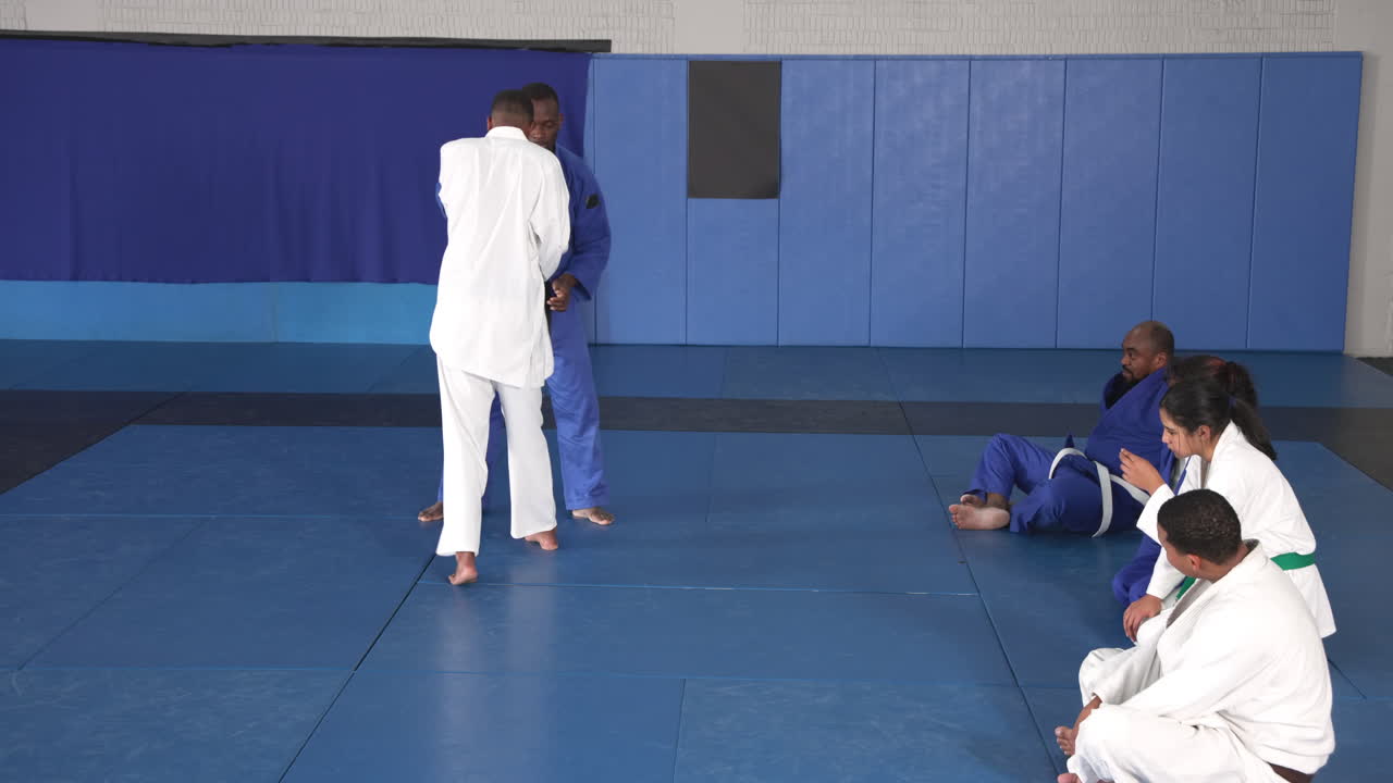 Practicing judo, two men sparring on mat while others watch attentively