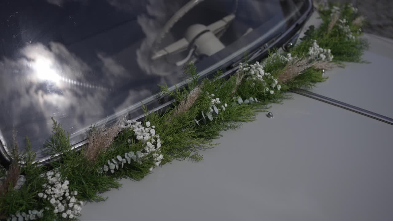 초록색과 흰색 꽃 화환으로 장식된 빈티지 웨딩카의 클로즈업 사진이에요