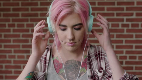 portrait of alternative punk woman with pink hair listening to music using headphones