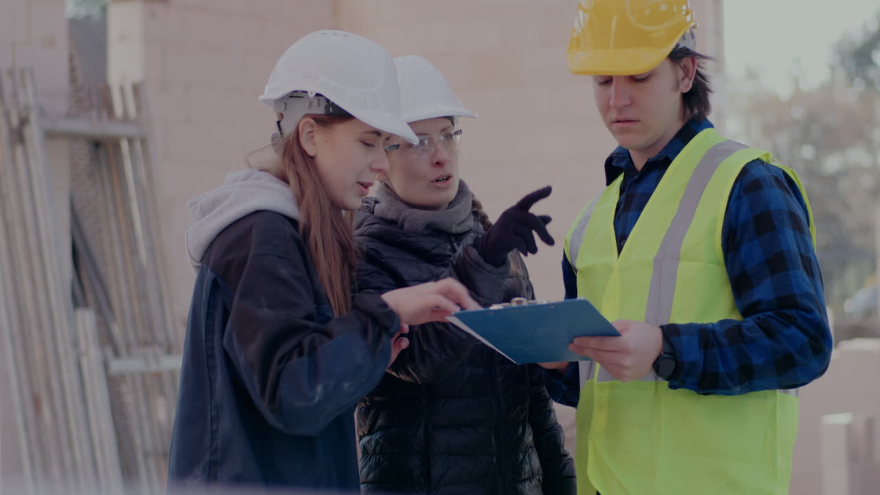 Confident young female architect and engineer discussing over clipboard with male coworker standing together at construction site