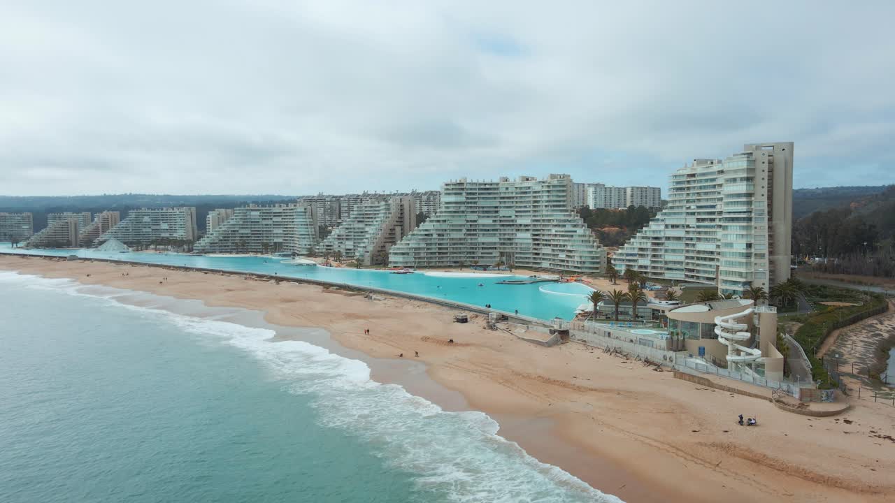 Aerial dolly out of sea and sand shore near world largest swimming pool and resorts in Algarrobo, Chile