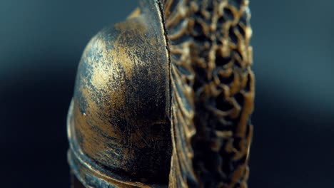 un primer plano macro cinematográfico de un diseño espartano, casco de bronce de metal guerrero, en un soporte giratorio, iluminación de estudio, video full hd, cámara lenta 120 fps