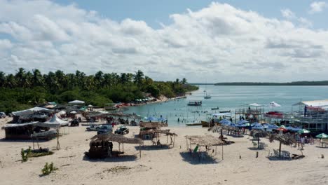 Dolly-in-aerial-drone-shot-flying-over-the-beautiful-tropical-touristy-Restinga-beach-where-the-large-Curimataú-river-meets-the-sea-near-Barra-do-Cunhaú-in-Rio-Grande-do-Norte,-Brazil-on-a-summer-day