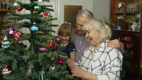 Children-girl-with-elderly-couple-grandparents-decorating-artificial-Christmas-pine-tree-at-home