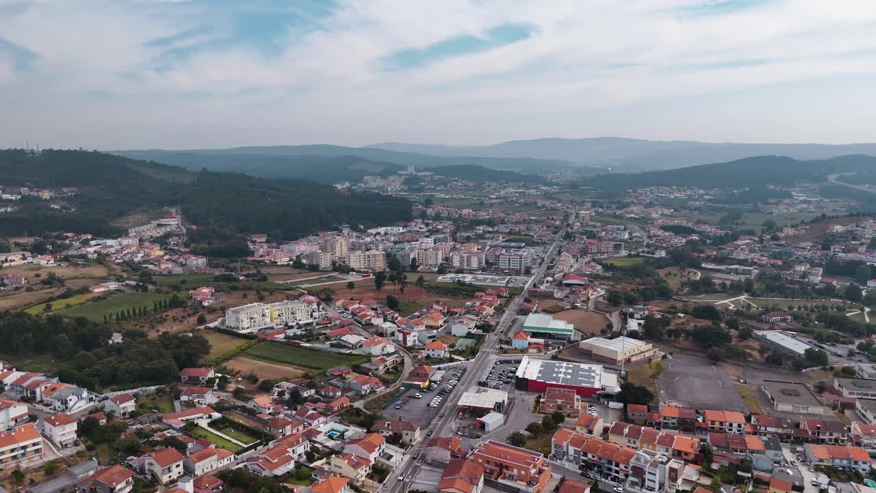 Vista aérea - rua principal atravessando a Vila de Alfena com casas, edifícios e colinas em Portugal.