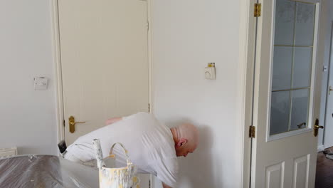 A skilled decorator applies white paint on a living room wall, revitalizing the space with a neat finish and attention to detail.