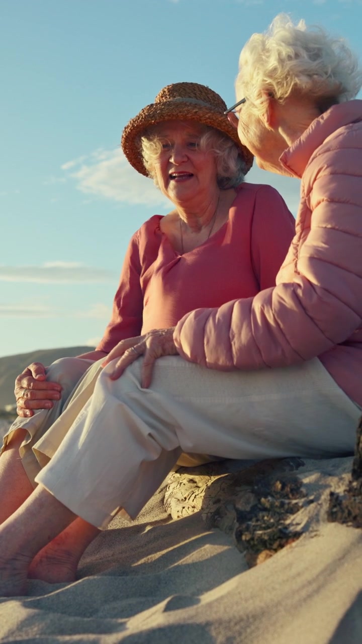 Due donne anziane che parlano sedute su una spiaggia sabbiosa