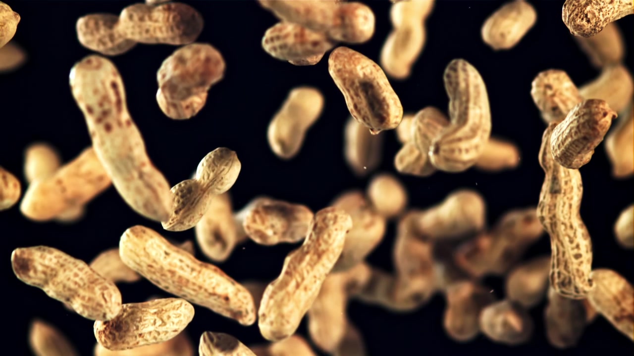Raw Peanuts Falling in Slow Motion Against a Black Background