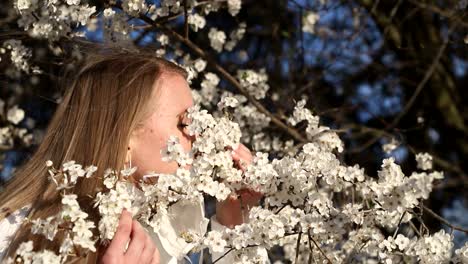 girl in white jacket photographs white color in spring using smartphone for photo blonde girl in a white mask makes a selfie on a background of flowering fruit trees photos for social networks