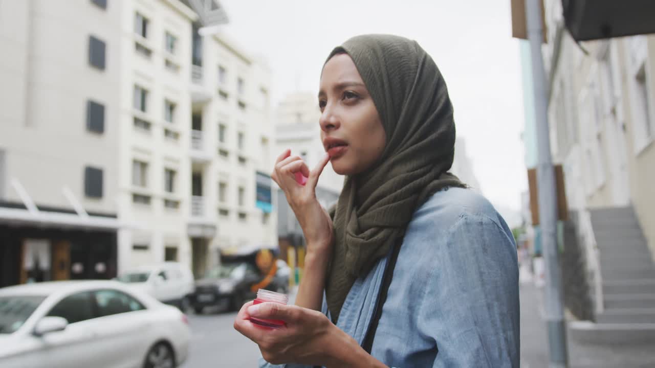 Woman wearing hijab putting lipstick in the street