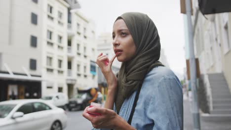 woman wearing hijab putting lipstick in the street