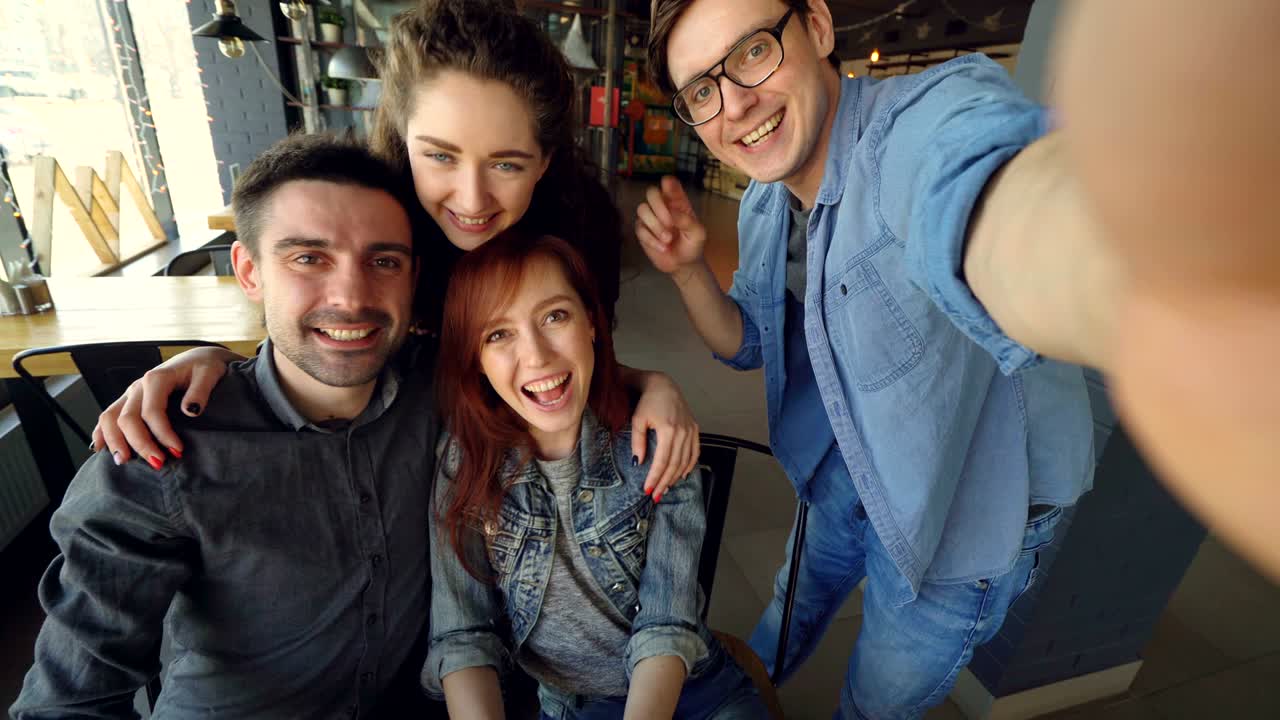 Toma en primera persona de amigos alegres haciéndose una selfie en una pizzería, posando y sonriendo, riendo y gesticulando juntos. Concepto de amistad y gente feliz