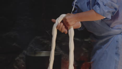 farmer woman wringing fresh cheese curd by stone fireplace with kettle