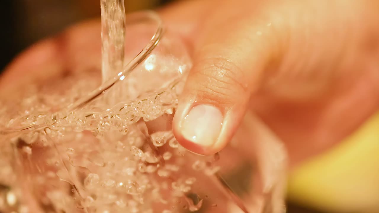 한 손 이 흐르는 물 으로 유리잔 을 청소 하고 있다