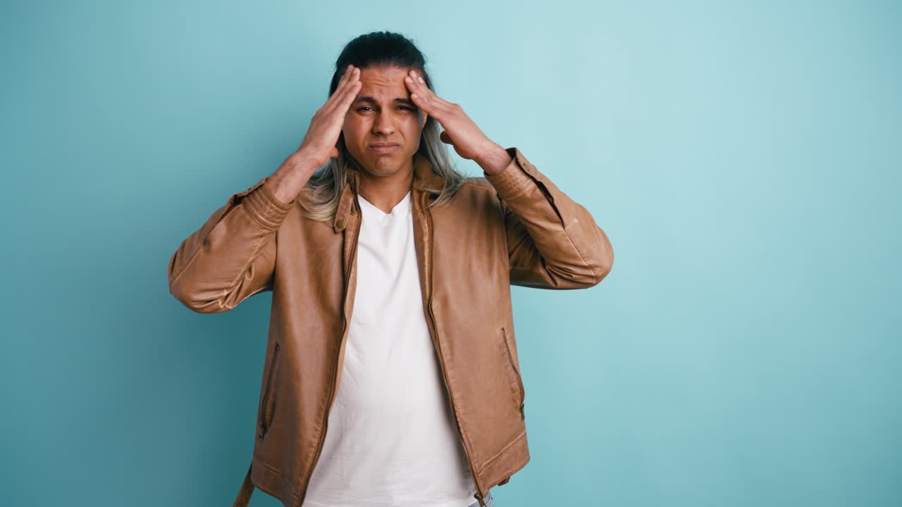 Young Man Suffering from a Headache Against a Blue Background