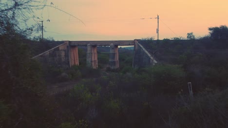 aerial drone shot of an abandoned old concrete railway bridge with dense forest hills in background during late evening time