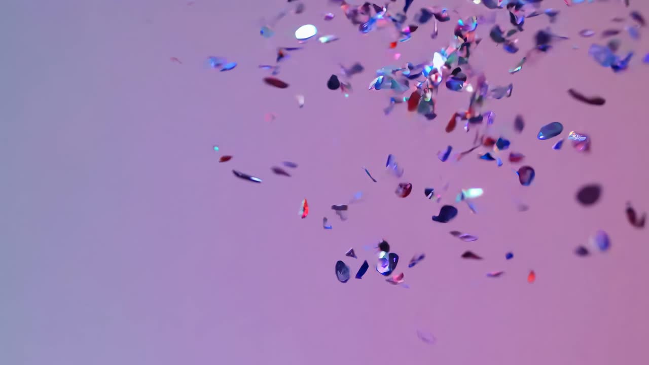 Aerial view of colorful confetti falling against a soft purple background, creating a festive