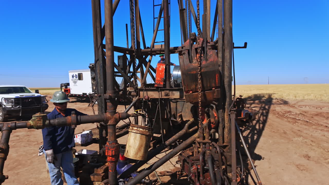 Man wearing a protective helmet stands at the foot of a derrick for oil production. Equipment for drilling natural resources in the desert.