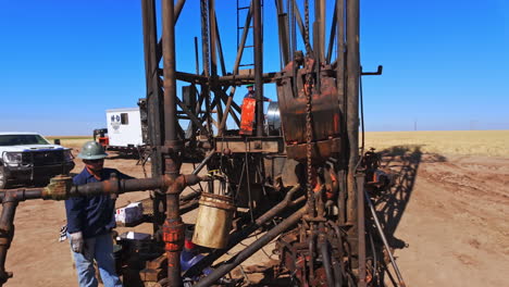 man wearing a protective helmet stands at the foot of a derrick for oil production. equipment for drilling natural resources in the desert.