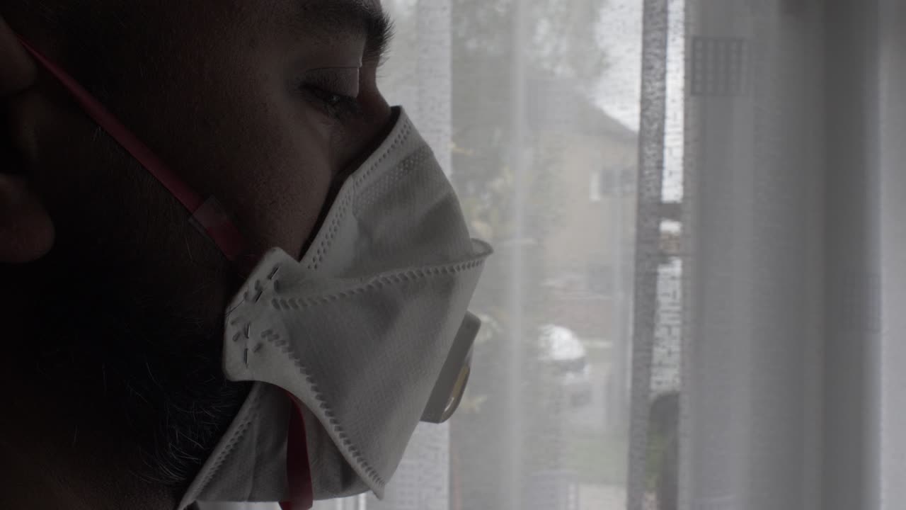 Adult Asian Male Wearing FFP Three Mask Indoors Looking Through Curtain
