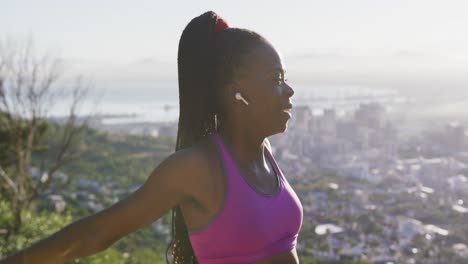 femme afro-américaine portant des écouteurs sans fil étendant ses bras à l'extérieur