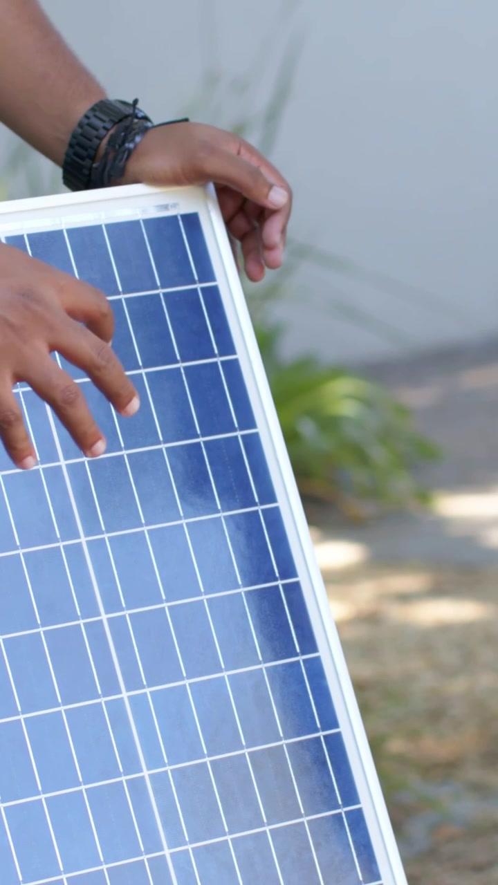Video verticale: Uomo in maglietta bianca che si aggiusta, mostra, inclina e indica un pannello solare all'esterno, con spazio per il testo.