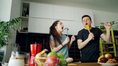 una pareja joven y alegre se divierten bailando y cantando mientras cocinan el desayuno en la cocina de casa.