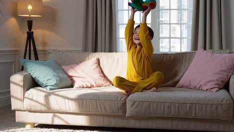 happy child playing with a dinosaur toy on the sofa