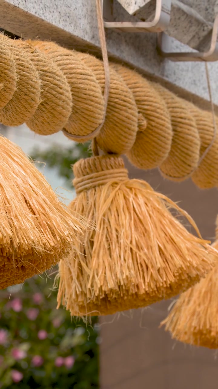 Una mano si protende per toccare nappe di paglia tradizionali che pendono da una corda sacra shimenawa.